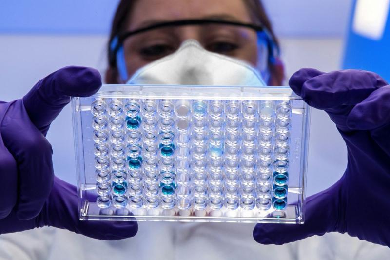 image of a lab worker wearing gloves, safety glasses, and mask reading a multi-well plate